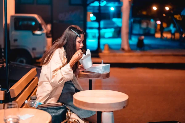 A menina está comendo fast food, na rua da cidade da noite — Fotografia de Stock