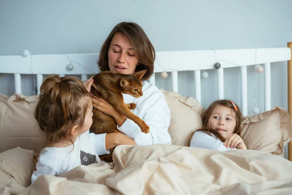 Happy mother and two daughters smiling hugs in bed — Stock Photo, Image