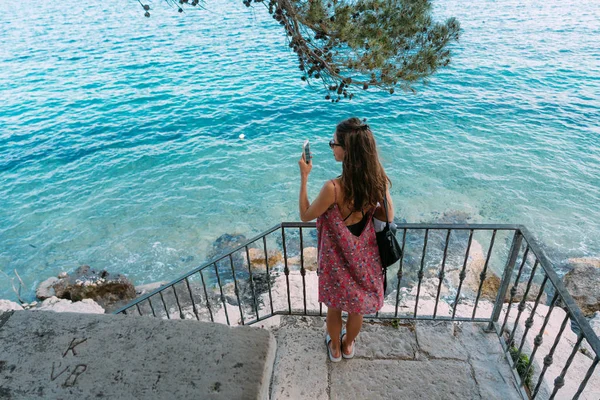 Uma linda menina junto ao mar tira uma foto — Fotografia de Stock