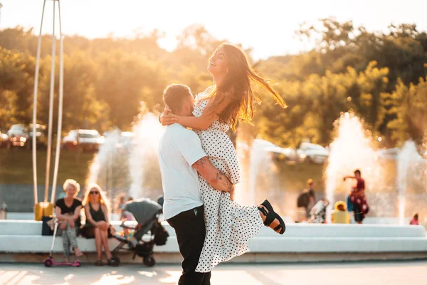 Handsome guy twists a beautiful girl on a background of a fountain — Stock Photo, Image