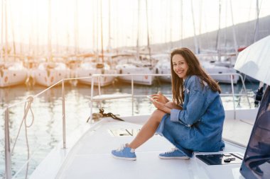 Genç güzel kız bir yat bir akıllı telefon ile güvertede oturuyor