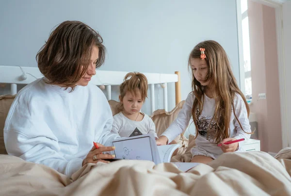 Anne ve iki kızı yatakta çizmek — Stok fotoğraf