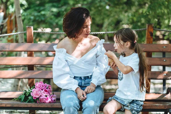 Mamma och hennes lilla dotter på en bänk i parken. — Stockfoto