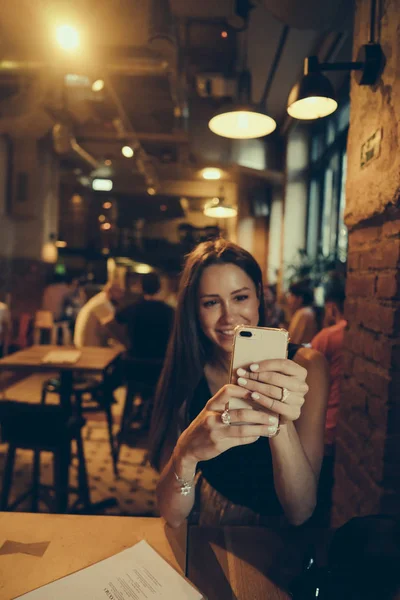 Хипстерская девушка держит в руках мобильный телефон во время отдыха в кафе — стоковое фото