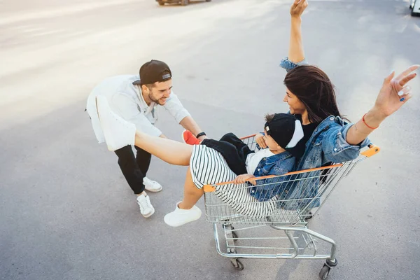 Young dad carries mom and son in a cart on the parking lot