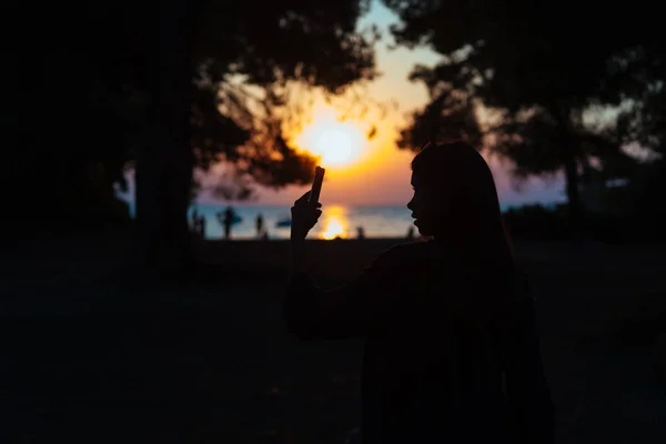 Mulher segurar e tocar smartphone sobre belo pôr do sol fundo no mar — Fotografia de Stock