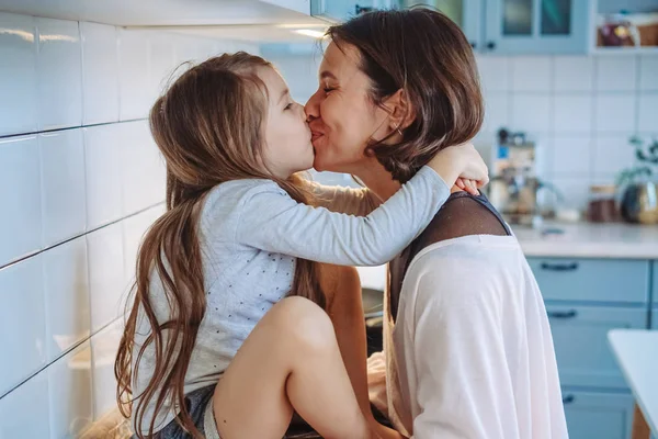 Mom kisses her little daughter in the kitchen