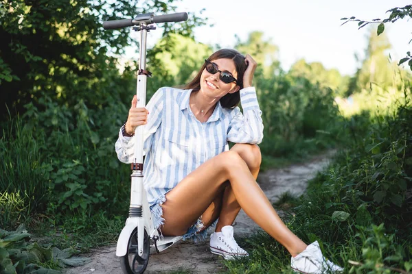 Menina com uma scooter na natureza posando para a câmera — Fotografia de Stock
