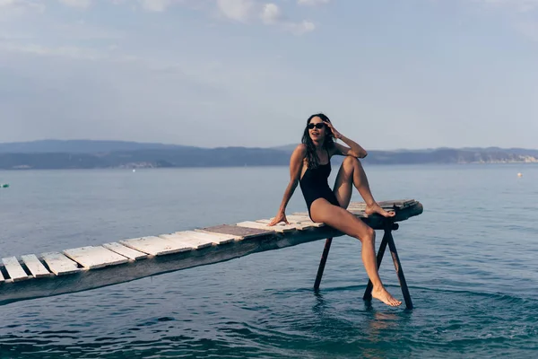 Attractive woman in a black swimsuit on the pier. — Stock Photo, Image