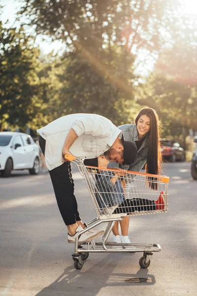 Les jeunes parents mettent leur fils dans un chariot et s'amusent dans le parking . — Photo