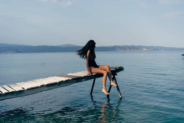 Attractive woman in a black swimsuit on the pier. — Stock Photo, Image