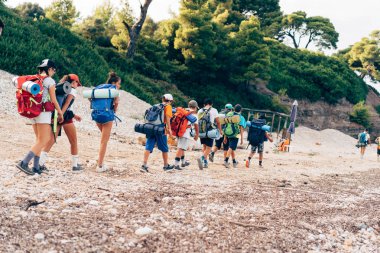 Deniz kıyısında kumlu bir yolda yürürken backpackers grup