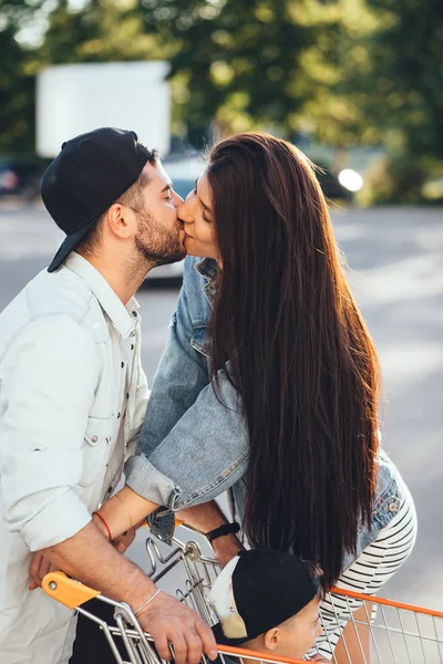 Junge, liebevolle Eltern küssen sich auf dem Parkplatz vor dem Supermarkt. — Stockfoto