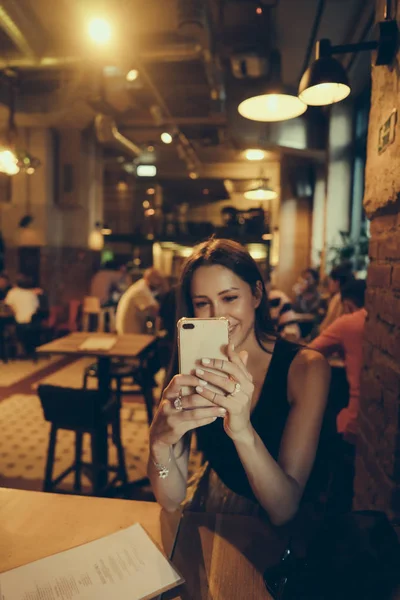 Hipster menina está segurando telefone celular em mãos durante o descanso no café — Fotografia de Stock