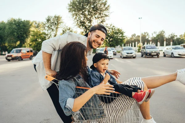 Young dad carries mom and son in a cart on the parking lot