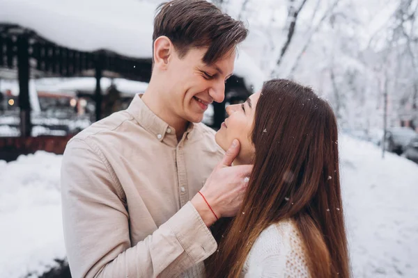 Cara jovem e menina bonita beijo em um parque nevado. Casal em camisolas . — Fotografia de Stock