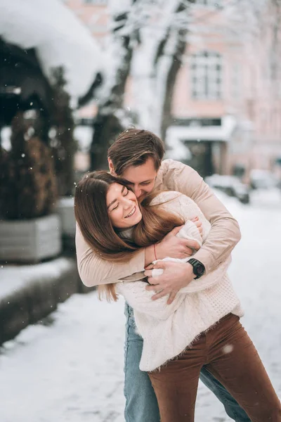 Ung kille och vacker flicka kiss i en snöig park. Par i tröjor. — Stockfoto