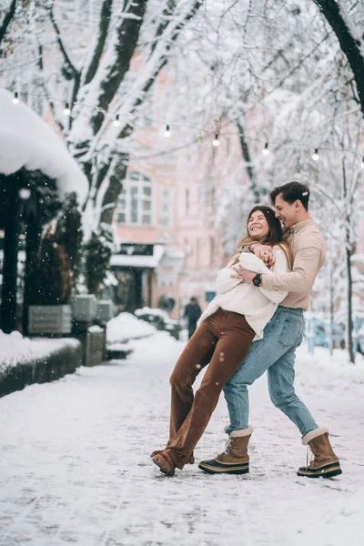 Cara jovem e menina bonita se divertir em uma rua nevada. Casal em camisolas . — Fotografia de Stock