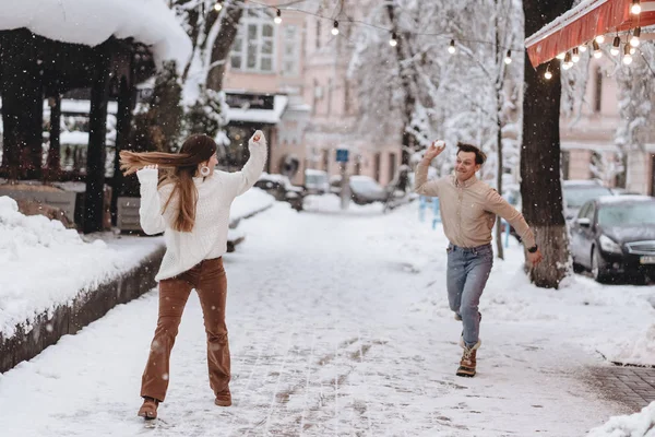 Joyful jovem casal em camisolas está jogando bolas de neve na rua . — Fotografia de Stock