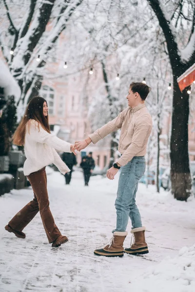 Cara jovem e menina bonita se divertir em uma rua nevada. Casal em camisolas . — Fotografia de Stock