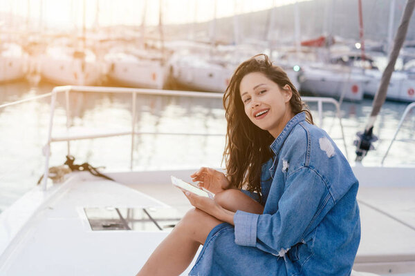 Young beautiful girl is sitting on the deck of a yacht with a smartphone