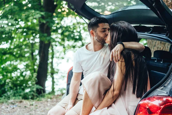 Una giovane coppia felice e 'seduta nel bagagliaio della loro auto. . — Foto Stock