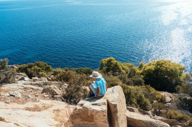deniz manzarası üzerinde arka plan ile bir kayaya oturan çocuk