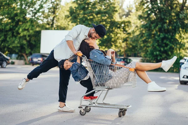 Young dad carries mom and son in a cart on the parking lot