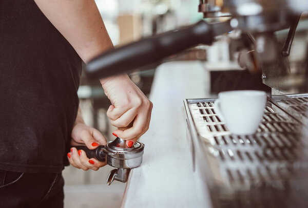 Barista presses ground coffee using tamper. Close-up view on hands