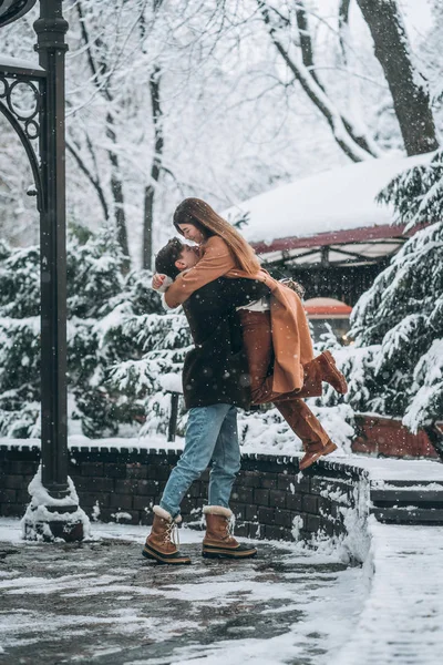 Jonge kerel en mooi meisje kussen in een besneeuwde park — Stockfoto