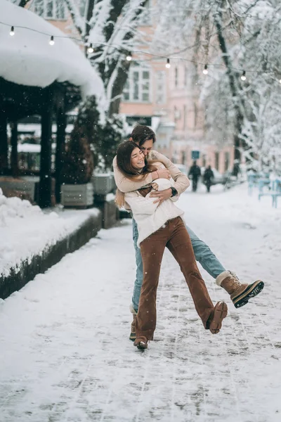 Jonge kerel en mooi meisje have fun op een besneeuwde straat. Paar in truien. — Stockfoto