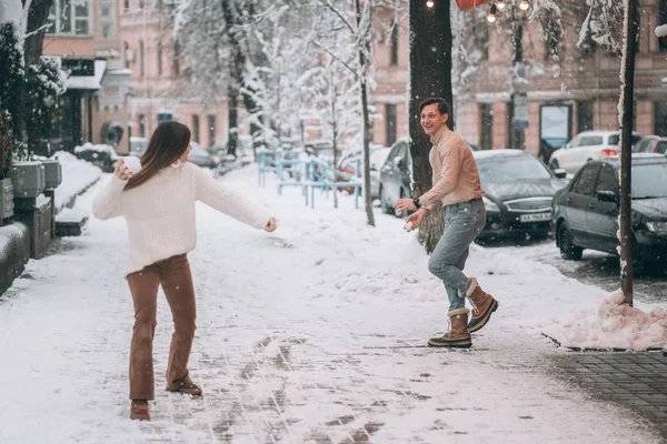 Joyful jovem casal em camisolas está jogando bolas de neve na rua . — Fotografia de Stock