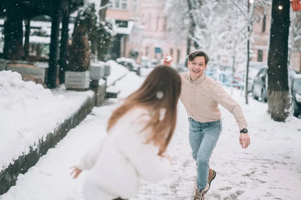 Alegre joven pareja en suéteres es jugando bolas de nieve en la calle . —  Fotos de Stock