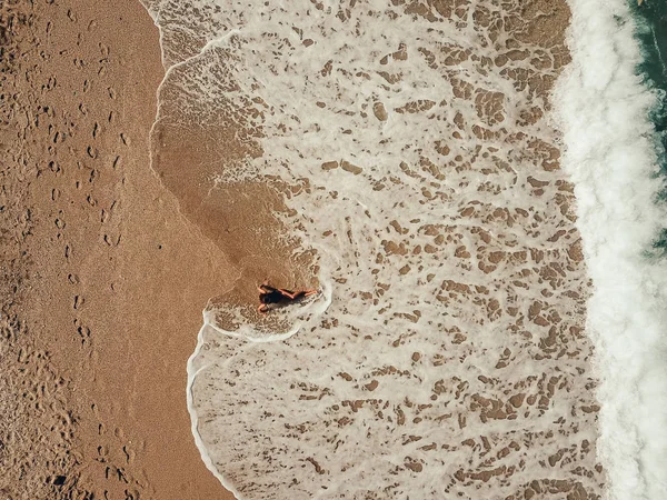 Вид сверху с воздуха молодая женщина лежит на песчаном пляже и волны — стоковое фото