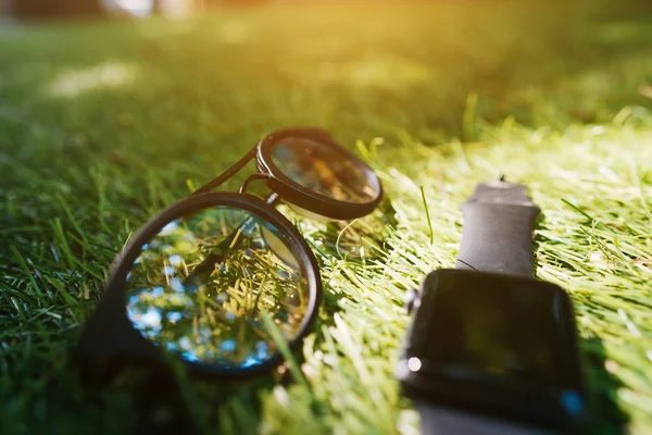 Slimme horloge en zonnebril liggen op het gras — Stockfoto