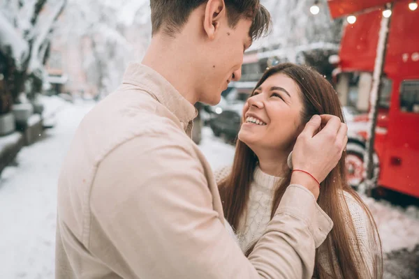 Cara jovem e menina bonita beijo em um parque nevado. Casal em camisolas . — Fotografia de Stock