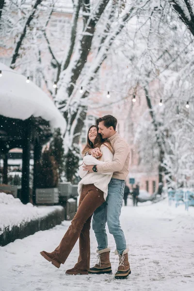 Jonge kerel en mooi meisje have fun op een besneeuwde straat. Paar in truien. — Stockfoto