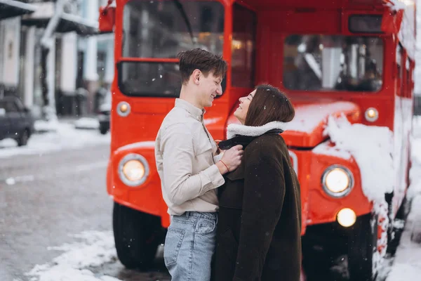 Ung kille värmer sin vackra flicka med jackan på en snöig gata — Stockfoto
