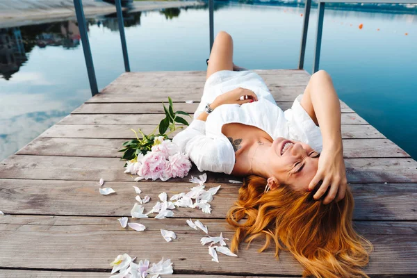Atraktivní mladá bokovky žena v bílých šatech leží na dřevěnou podlahu. — Stock fotografie