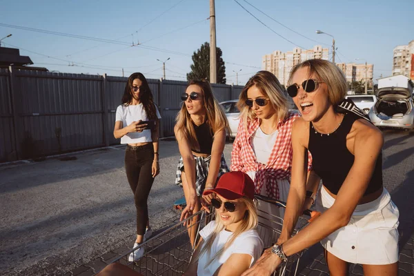 Πέντε νεαρά κορίτσια να διασκεδάσουν με ένα καρότσι σούπερ μάρκετ σε ένα πάρκο αυτοκινήτων — Φωτογραφία Αρχείου