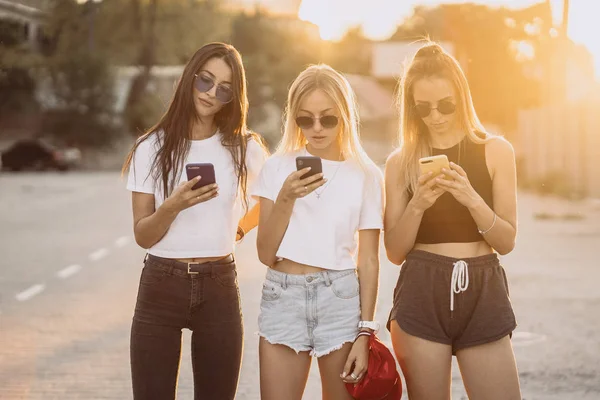 Tre attraktiva kvinnor står på parkering med smartphones — Stockfoto