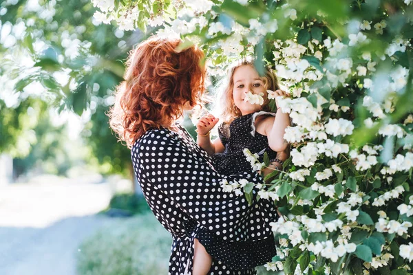 Young woman stands near jasmine with a small daughter — Stock Photo, Image