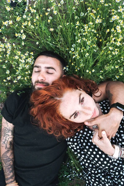 Junges Paar liegt mit Gänseblümchen auf dem Feld. — Stockfoto