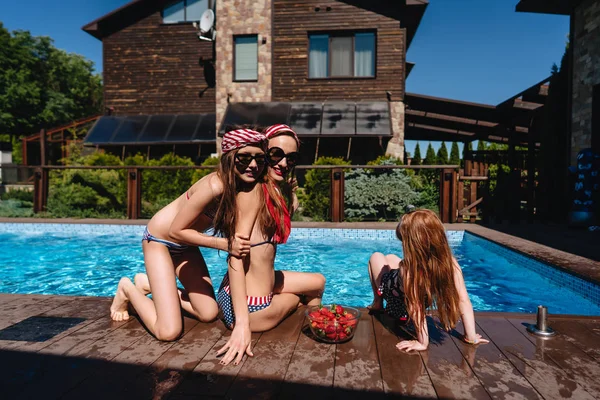 Happy mother and two daughters in swimsuits at border of pool. — Stock Photo, Image