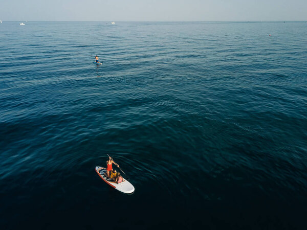 Mother with two daughters stand up on a paddle board. At sea, calm.