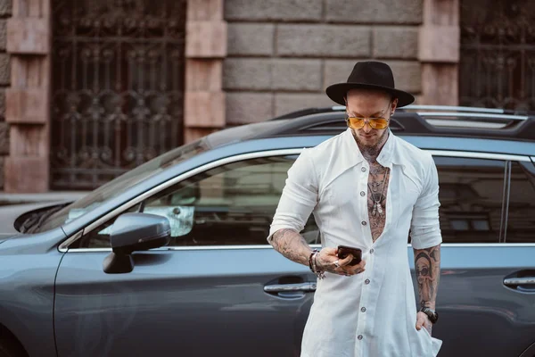 Un joven con sombrero y gafas de sol sostiene un teléfono móvil en sus manos — Foto de Stock