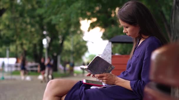 Молодая женщина, одетая небрежно, работает на скамейке в парке . — стоковое видео