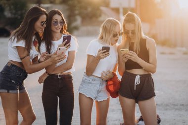 Dört çekici kadın akıllı telefonlarıyla araba parkında duruyorlar.