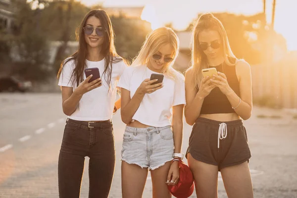 Tre attraktiva kvinnor står på parkering med smartphones — Stockfoto