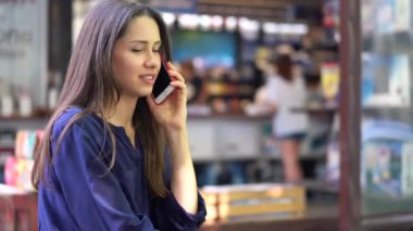 Sokak bir kafede Mobil cep telefonuyla konuşan genç esmer kız